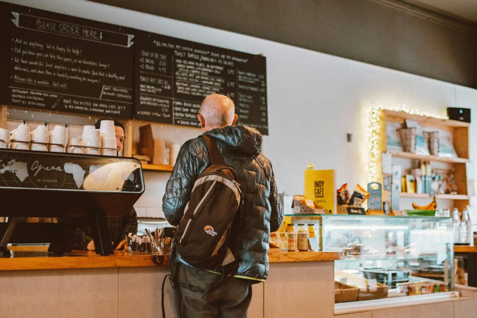 Male in line at a coffeee shop looking at the menu display.